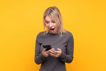 Fototapeta premium Young blonde woman over isolated yellow background surprised and sending a message
