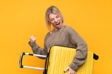 Young blonde woman over isolated yellow background in vacation with travel suitcase