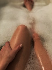 Woman legs and hand in the bathtub with foam