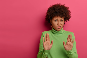 Awkward unimpressed woman with Afro hairstyle, pulls palms towards camera, refuses something,...