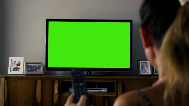 Woman Watching a TV with Green Screen at Home. You can replace green screen with the footage or picture you want. You can do it with “Keying” effect in After Effects.