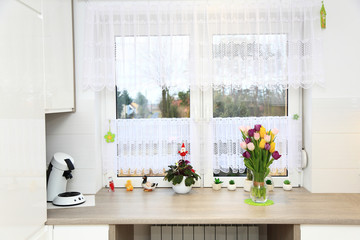 Klorowe tulipany w wazonie na parapecie białego wspłóczesnego okna w jasnej kuchni.