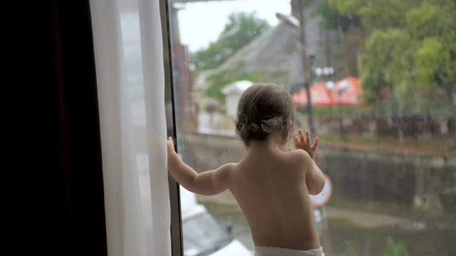 Toddler girl in diaper standing on the background of the panoramic window