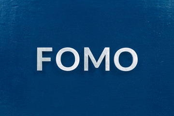 the abbreviation word fomo - fear of missing out - laid with silver letters on classic blue color...