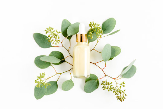 Bottle with hyaluronic acid / eucalyptus essential oil, eucalypt leaf on white background. Concept of modern beauty. Natural / Organic cosmetics products. Flat lay, top view.
