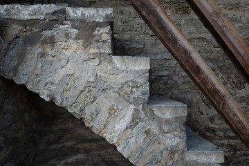 Side view on the steps of an old stone staircase in a medieval fortress. A fragment of a wooden railing is visible. Background. Texture.