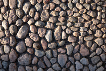 Vintage pavement made of small cobblestones of gray granite. Part of the space is lit by the sun, another part is in the shade. Background. Texture.