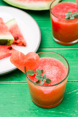 Fresh watermelon blended drink with mint leaves and a heart of watermelon in glasses and slices of watermelon on a wooden table. Ready-to-eat drink