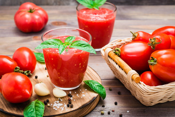 Appetizing fresh tomato juice with basil leaves in glasses and ingredients for its preparation on a wooden table