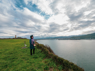 Fototapeta premium Woman in a coat looking at the sea and the port of Bilbao in the distance.