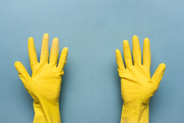 Female hand in yellow glove is holding copy space on blue background.