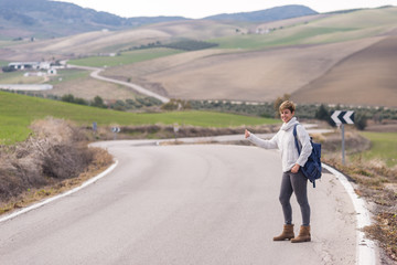 Obraz premium Woman with backpack hitchhiking on a lonely rural road.