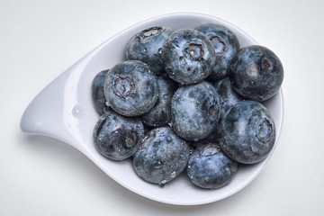 Fresh and healthy blueberries in a small porcelain dish on white background.