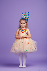 Children's birthday party, masquerade. Little happy toddler child girl in a puffy tutu fancy dress, having fun on Violet background. Space for text