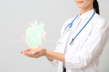 Female cardiologist holding drawn heart on light background