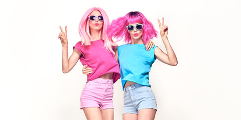 Two Young carefree Woman with stylish pink hair, in shorts jump dance. Beautiful fashionable model girl in colorful summer outfit. Joyful friends with fashion pink hairstyle dancing on white