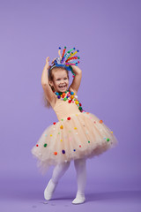Children's birthday party, masquerade. Little happy toddler child girl in a puffy tutu fancy dress, having fun on Violet background. Space for text
