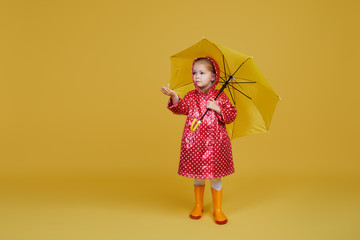 Cheerful child girl with yellow umbrella and red rain coat on colored yellow background. Copy space for text