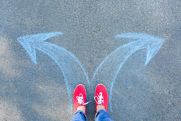 Person standing on road with arrows pointing in different directions. Concept of choice