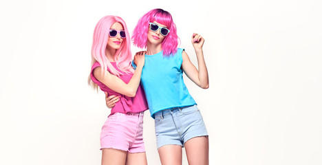 Two fashionable girl having fun in studio. Beautiful embracing young woman in Stylish summer colorful outfit, Trendy dyed pink hair. Glamour funny model sister, pink fashion hairstyle on white, banner