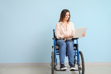 Handicapped young woman with laptop near color wall