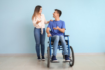 Fototapeta na wymiar Handicapped young man in wheelchair and his wife near color wall