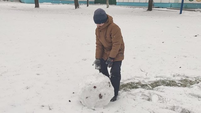 Boy rolls a big ball of snow for a snowman