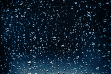 Glass covered with drops of water on a dark background, blurred background in blue tonality.