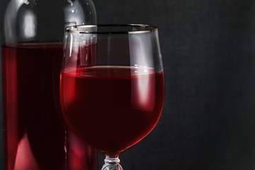 Bottle and glass of red wine on the table on a dark background.