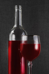Bottle and glass of red wine on the table on a dark background.