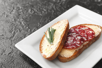 Plate with tasty bread, butter and sausages on dark background