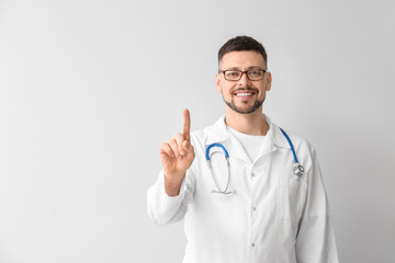 Male cardiologist with raised index finger on light background