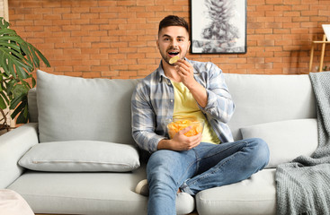 Handsome young man with tasty potato chips at home