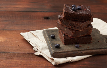 stack of square baked slices of brownie chocolate cake with walnuts on a wooden surface