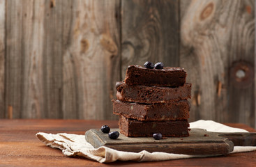 stack of square baked slices of brownie chocolate cake with walnuts on a wooden surface
