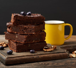 stack of square baked slices of brownie chocolate cake with walnuts on a wooden surface