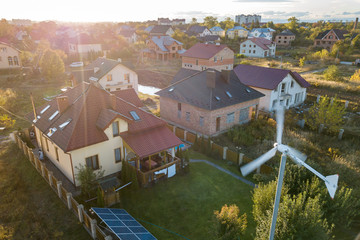 Aerial view of a residential private house with solar panels on roof and wind generator turbine.