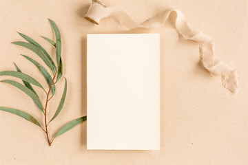 Fototapeta premium Mockup invitation, blank greeting card and green leaves eucalyptus. Flat lay, top view.