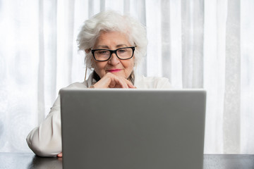 old lady with glasses looking at a computer on a wooden table.