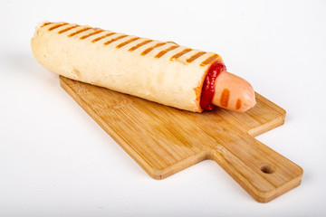 Tasty French hot-dog with ketchup arranged on a wooden board. A hot snack sold at gas stations.