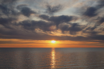 Golden sunset with lots of clouds above water horizon.