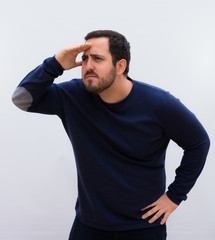 young handsome man looking bewildered and astonished, with hand over forehead looking far away, watching or searching against white wall.