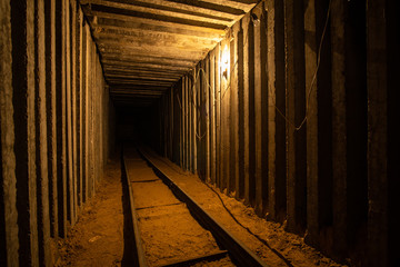 Empty underground square tunnel with rails for minecart and warm tungsten lighting. 