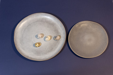 Gray handmade ceramic plates with quail eggs on classic blue background