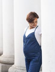 Fototapeta na wymiar Stylish Pregnant Woman Poses Among White Columns