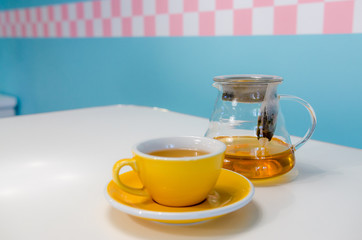 Yellow cup of tea and glass teapot on the table. Blue background
