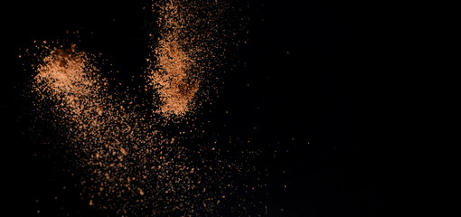 Fototapeta na wymiar Cocoa powder explosion in motion on black background. Chocolate dust. Wide banner.