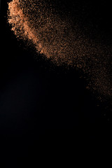 Fototapeta na wymiar Cocoa powder explosion in motion on black background. Chocolate dust.
