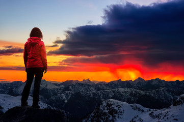 Obraz premium Adventurous Girl watching the Beautiful Dramatic Sunset on top of the Mountains. Composite Image with Landscape taken in BC, Canada. Concept: Adventure, Art, Travel, Hike, Outdoors, Explore