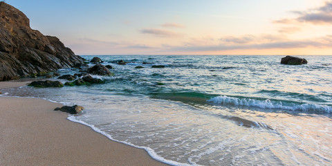 sunrise on the beach. beautiful summer scenery. rocks on the sand. calm waves on the water. clouds on the sky. wide panoramic view